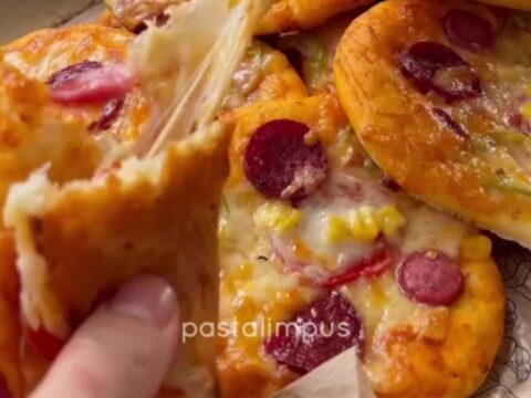 Golden mini pizzas with melted mozzarella, sucuk slices, and bell peppers on a baking sheet.