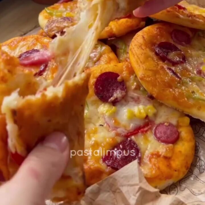 Golden mini pizzas with melted mozzarella, sucuk slices, and bell peppers on a baking sheet.
