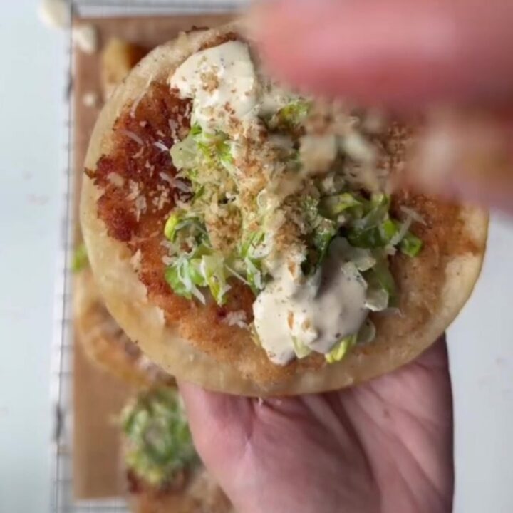 Crispy panko chicken smash tacos topped with Caesar slaw and shaved parmesan, on a wooden board