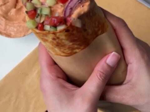A toasted chicken kebab wrap cut in half, showing juicy spiced chicken, charred peppers, and creamy garlic yogurt sauce.