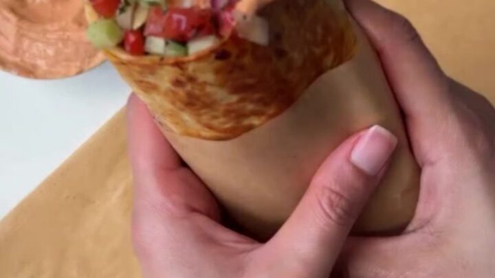 A toasted chicken kebab wrap cut in half, showing juicy spiced chicken, charred peppers, and creamy garlic yogurt sauce.