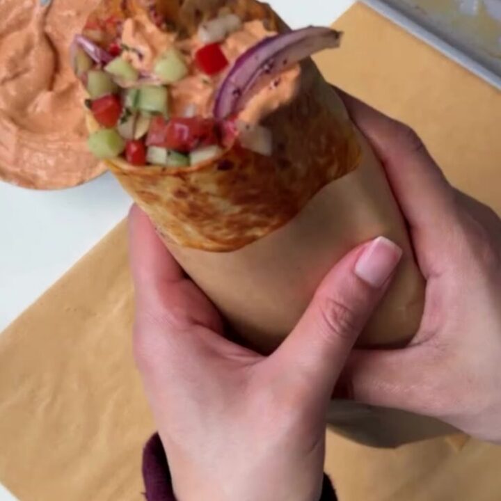 A toasted chicken kebab wrap cut in half, showing juicy spiced chicken, charred peppers, and creamy garlic yogurt sauce.