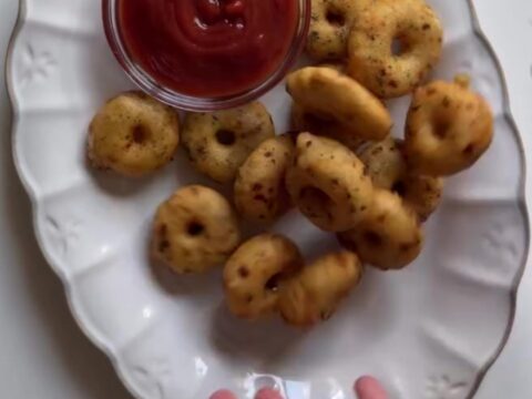 Golden crispy potato rings piled on a plate with a small bowl of spicy mayo for dipping
