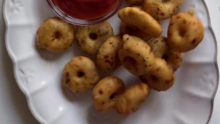 Golden crispy potato rings piled on a plate with a small bowl of spicy mayo for dipping