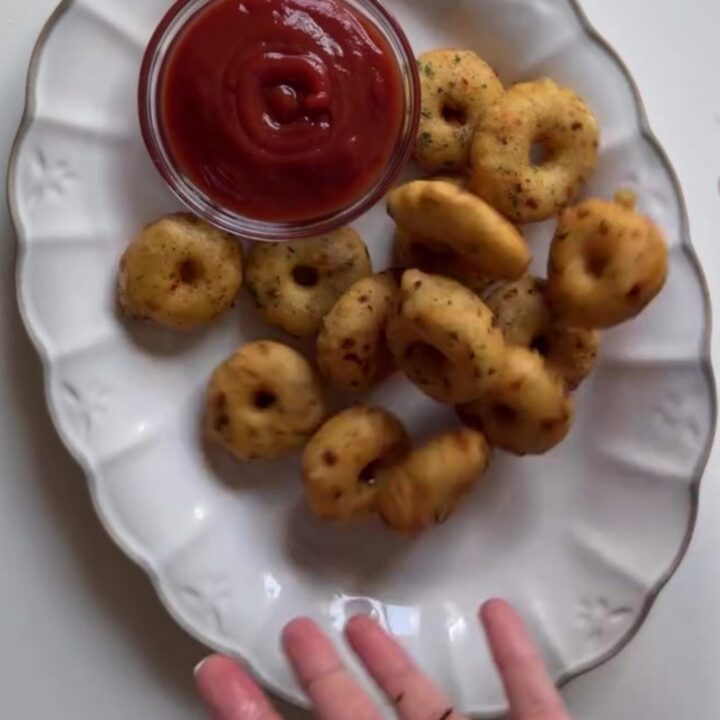 Golden crispy potato rings piled on a plate with a small bowl of spicy mayo for dipping