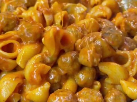 Skillet with stuffed pasta shells and meatballs topped with melted cheese and fresh basil.