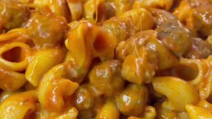 Skillet with stuffed pasta shells and meatballs topped with melted cheese and fresh basil.