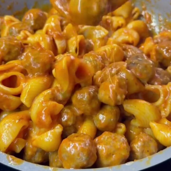 Skillet with stuffed pasta shells and meatballs topped with melted cheese and fresh basil.