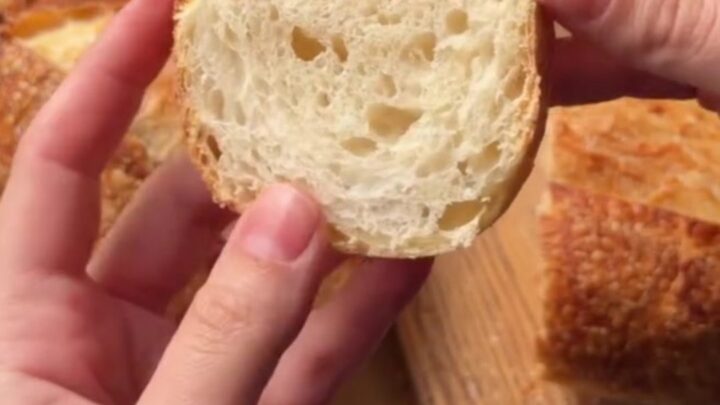 A dark golden sourdough boule with a blistered crust, sliced to show an open airy crumb