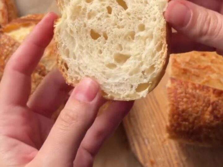 A dark golden sourdough boule with a blistered crust, sliced to show an open airy crumb