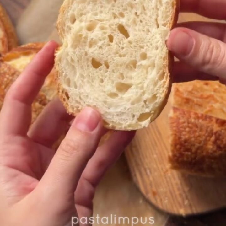 A dark golden sourdough boule with a blistered crust, sliced to show an open airy crumb