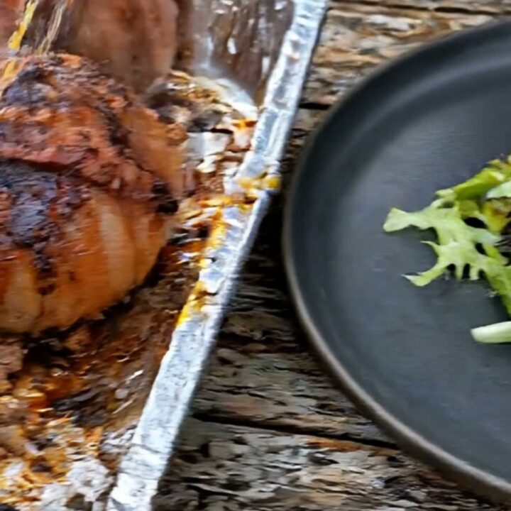 A close-up shot of a bacon-wrapped onion bomb with melting cheese pulling away from the juicy beef center.