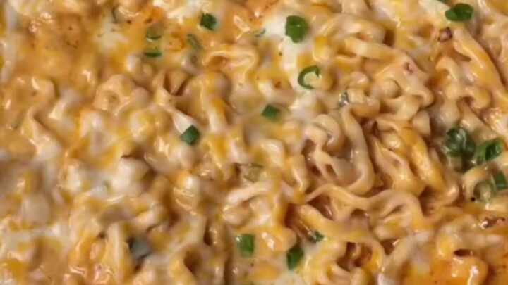 A bowl of creamy garlic chili ramen with glossy noodles, melted cheese sauce, and scallions.