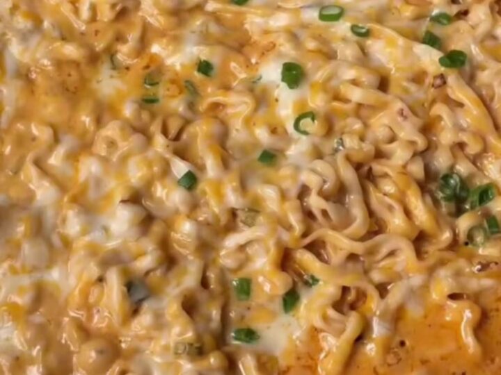 A bowl of creamy garlic chili ramen with glossy noodles, melted cheese sauce, and scallions.