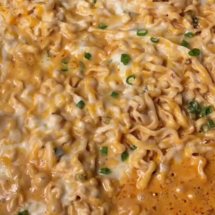 A bowl of creamy garlic chili ramen with glossy noodles, melted cheese sauce, and scallions.