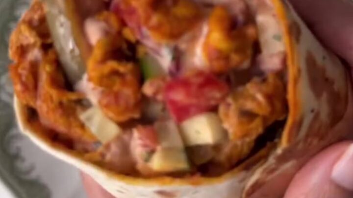 A crispy chicken shawarma wrap cut in half, showing layers of chicken, fries, pickles, and garlic sauce.