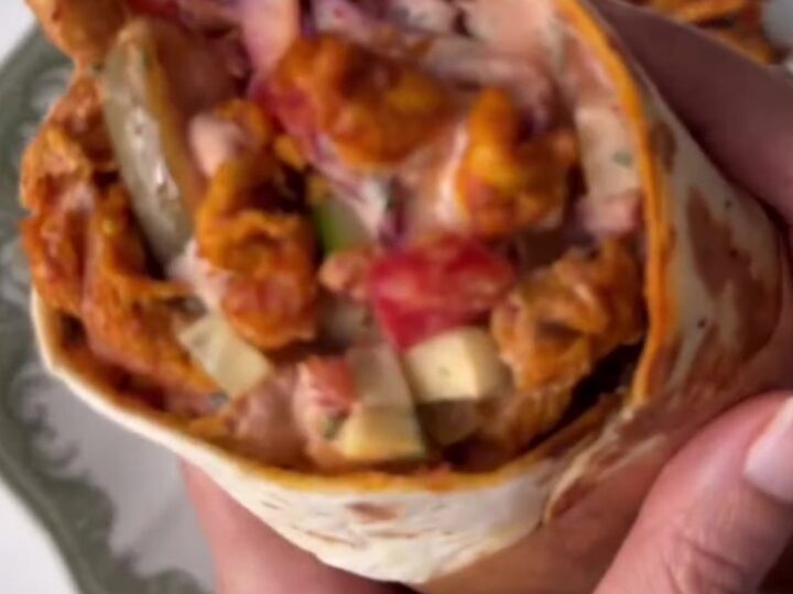 A crispy chicken shawarma wrap cut in half, showing layers of chicken, fries, pickles, and garlic sauce.
