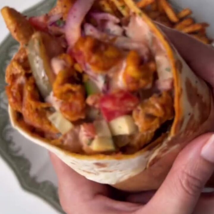 A crispy chicken shawarma wrap cut in half, showing layers of chicken, fries, pickles, and garlic sauce.