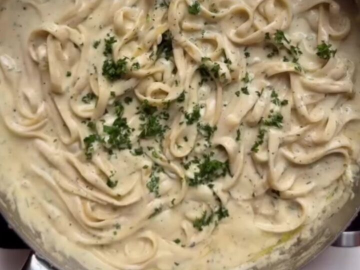 Fettuccine Alfredo in a white bowl with parsley and black pepper