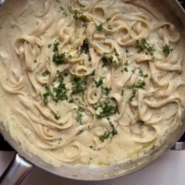 Fettuccine Alfredo in a white bowl with parsley and black pepper