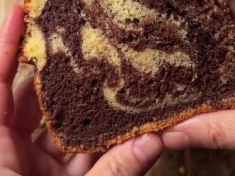 A golden marble loaf cake with a zebra swirl, dusted with powdered sugar, on a wooden board.