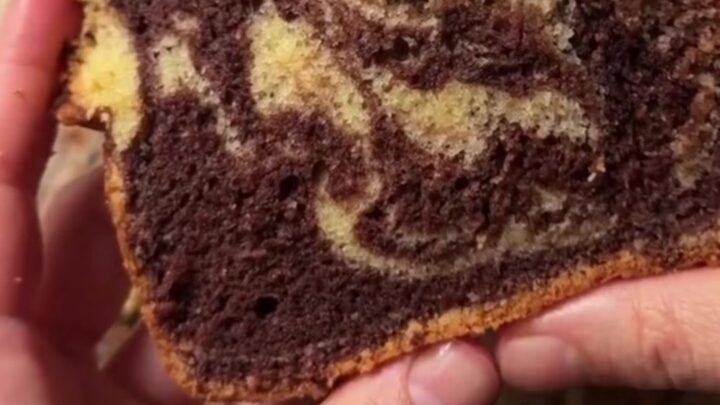A golden marble loaf cake with a zebra swirl, dusted with powdered sugar, on a wooden board.