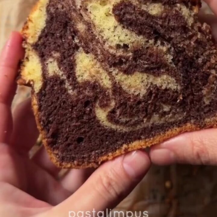 A golden marble loaf cake with a zebra swirl, dusted with powdered sugar, on a wooden board.