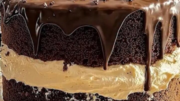 A two-layer chocolate cake on a glass stand with glossy ganache dripping down the sides.