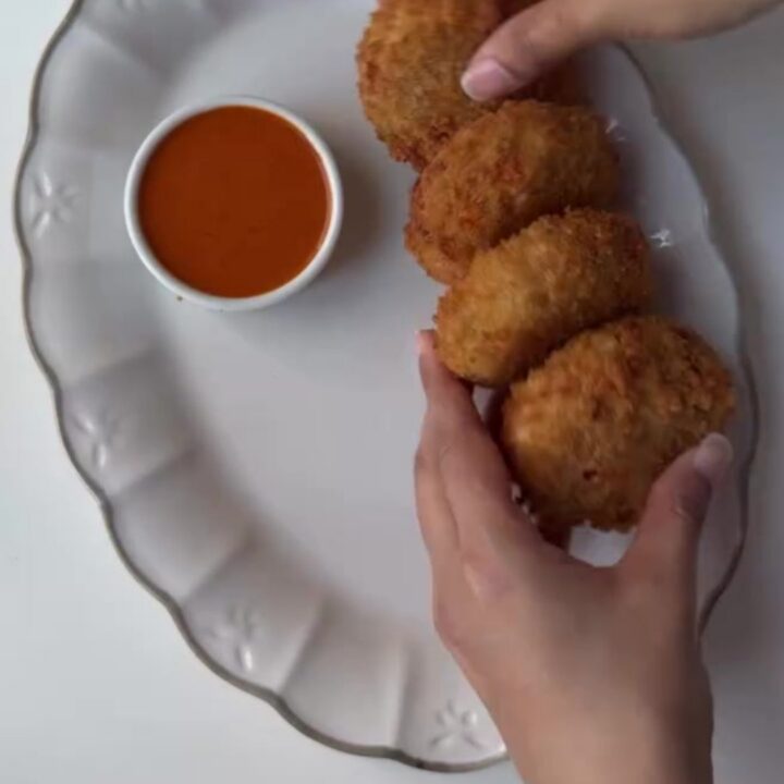 Crispy golden chicken potato croquettes piled on a plate with a bowl of creamy chipotle dip