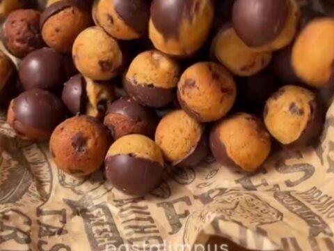 A pile of chocolate cookie truffles with white chocolate drizzle and cookie crumbs on a parchment-lined tray.