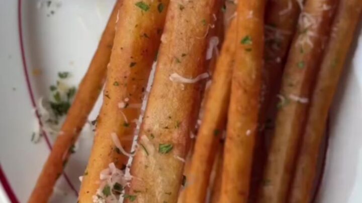 A pile of golden, extra-long fries coated in garlic butter and parmesan, served with a bowl of spicy mayo