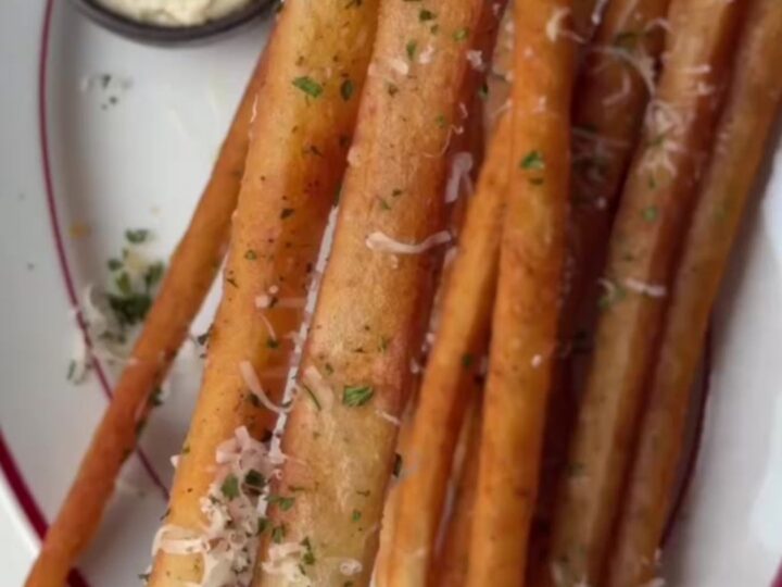 A pile of golden, extra-long fries coated in garlic butter and parmesan, served with a bowl of spicy mayo