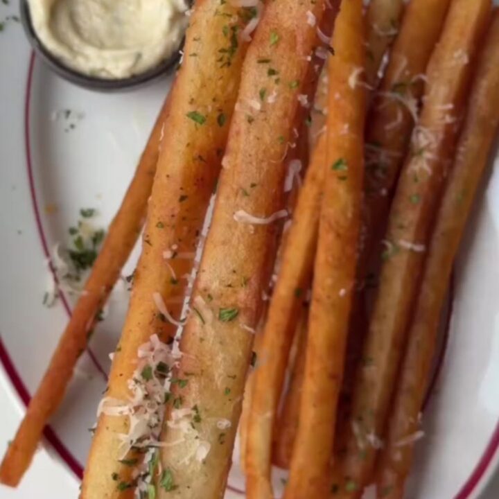 A pile of golden, extra-long fries coated in garlic butter and parmesan, served with a bowl of spicy mayo