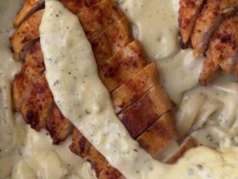 A fork twirling fettuccine with lemon garlic cream sauce, topped with sliced chicken breast and fresh parsley.