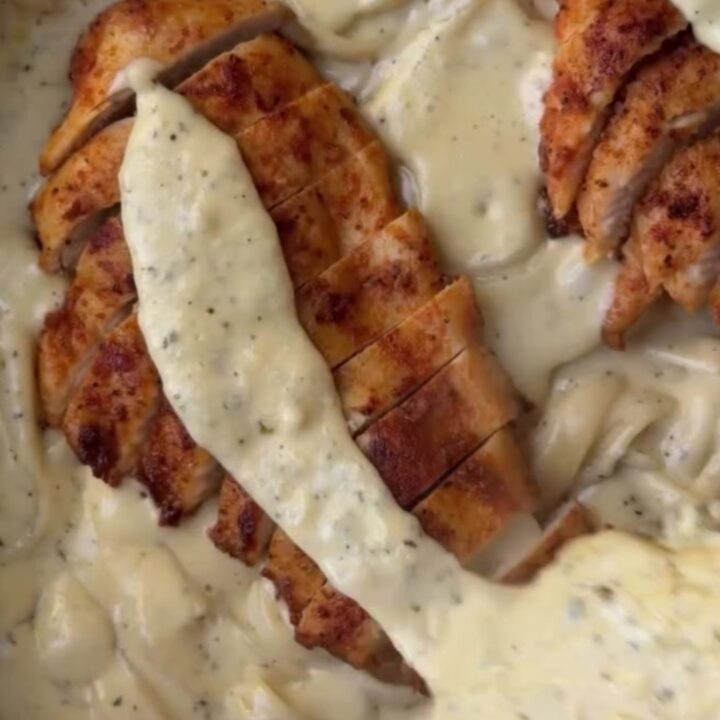 A fork twirling fettuccine with lemon garlic cream sauce, topped with sliced chicken breast and fresh parsley.