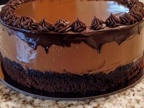 A slice of decadent chocolate mousse cake with a glossy ganache top on a plate.