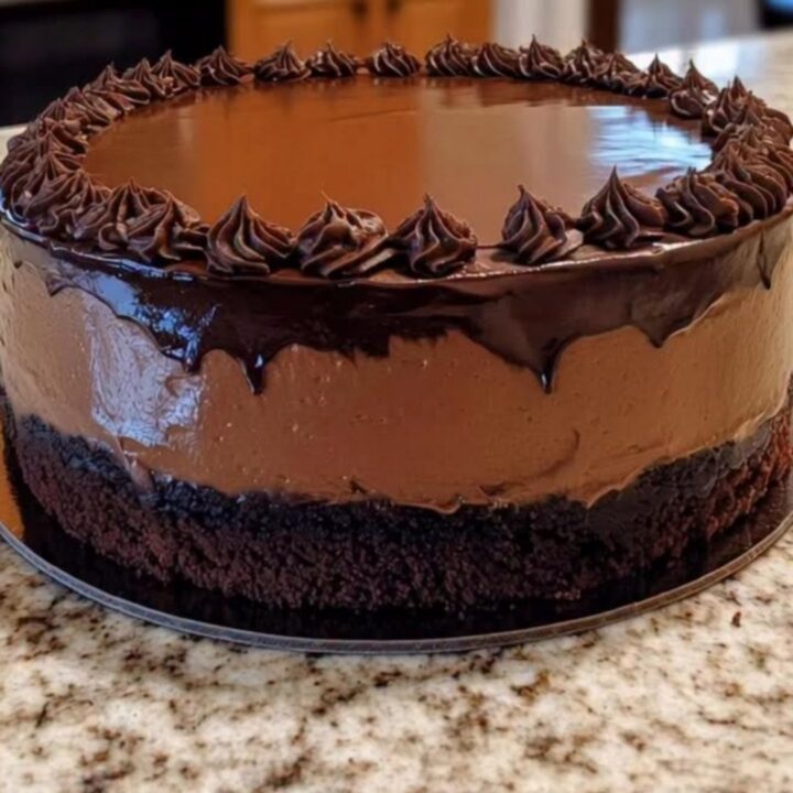 A slice of decadent chocolate mousse cake with a glossy ganache top on a plate.