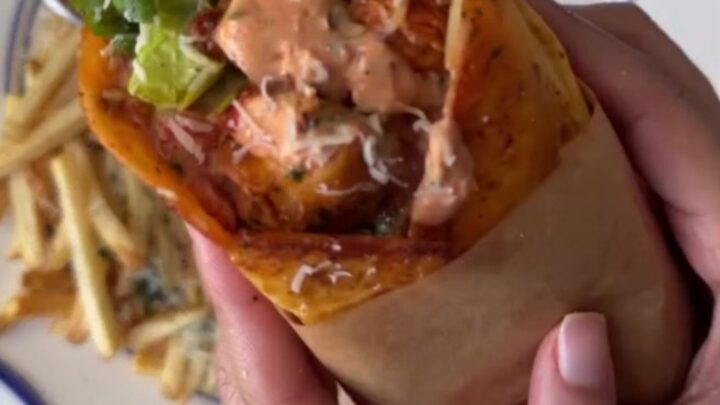 A crispy garlic parmesan chicken wrap cut diagonally, showing melted cheese and chicken, with a side of garlic mayo.