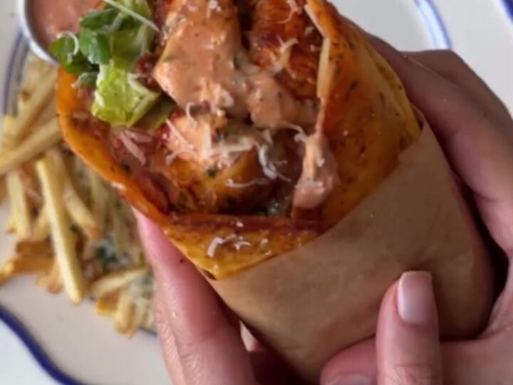 A crispy garlic parmesan chicken wrap cut diagonally, showing melted cheese and chicken, with a side of garlic mayo.