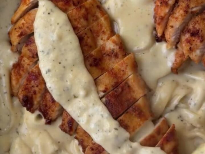 A fork twirling fettuccine in a creamy lemon garlic sauce, topped with sliced chicken breast and fresh parsley.