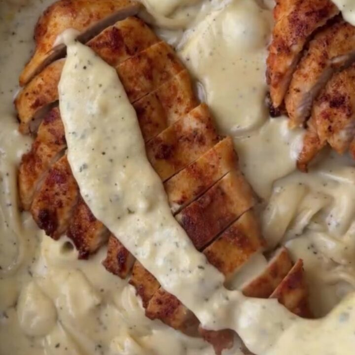 A fork twirling fettuccine in a creamy lemon garlic sauce, topped with sliced chicken breast and fresh parsley.