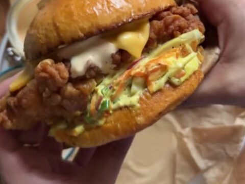 A tall fried chicken sandwich on a toasted brioche bun with pickles and spicy mayo, showing the craggy golden crust.