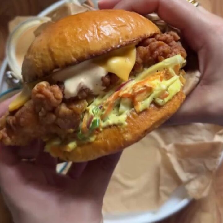 A tall fried chicken sandwich on a toasted brioche bun with pickles and spicy mayo, showing the craggy golden crust.