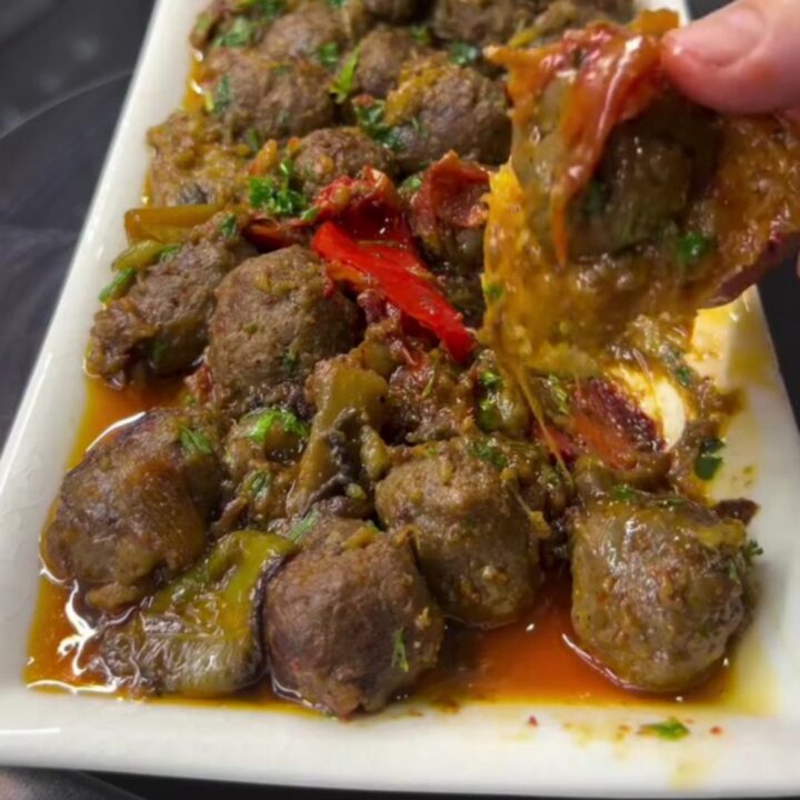 Skillet with eggplant and meatballs in tomato sauce, garnished with parsley, with crusty bread on the side.