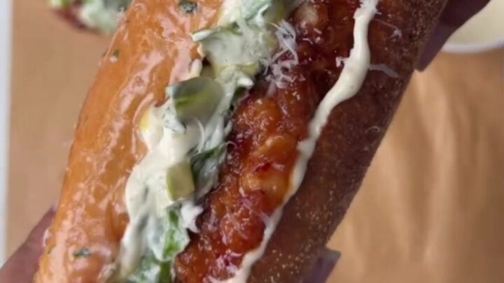 A crispy chicken Caesar sandwich with hot honey glaze on a toasted brioche bun, with romaine and parmesan peeking out