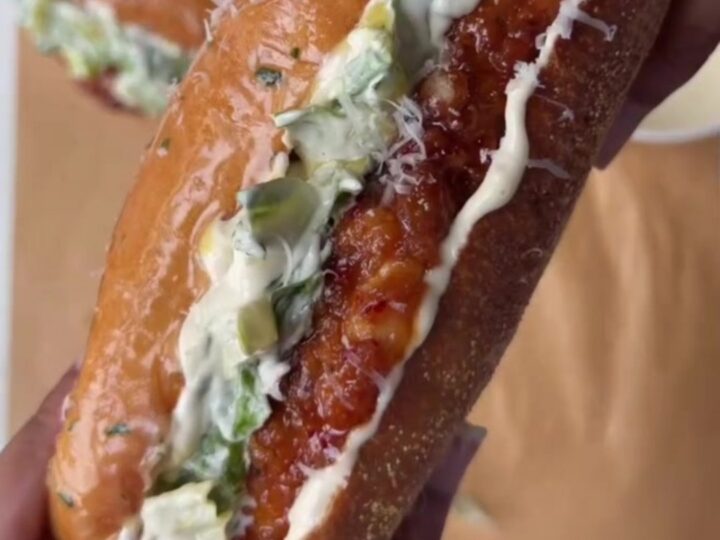 A crispy chicken Caesar sandwich with hot honey glaze on a toasted brioche bun, with romaine and parmesan peeking out