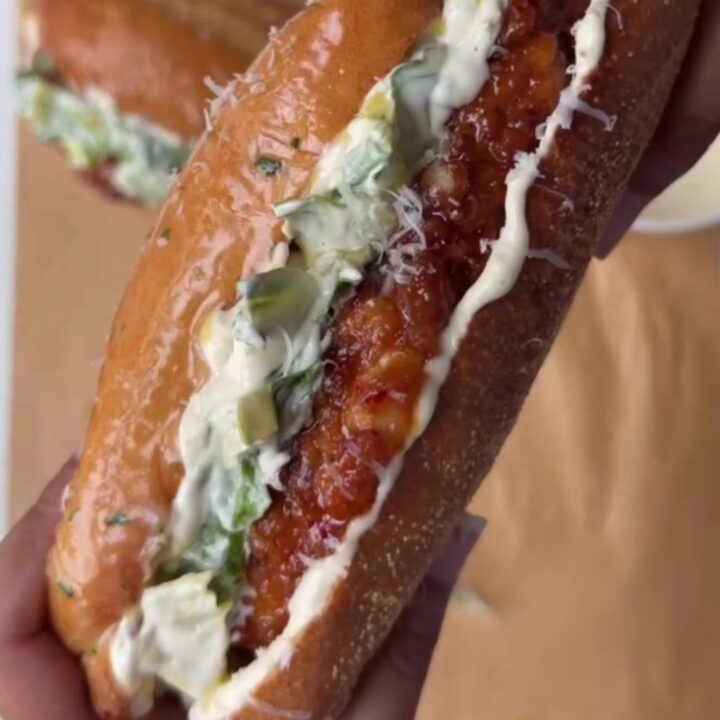 A crispy chicken Caesar sandwich with hot honey glaze on a toasted brioche bun, with romaine and parmesan peeking out