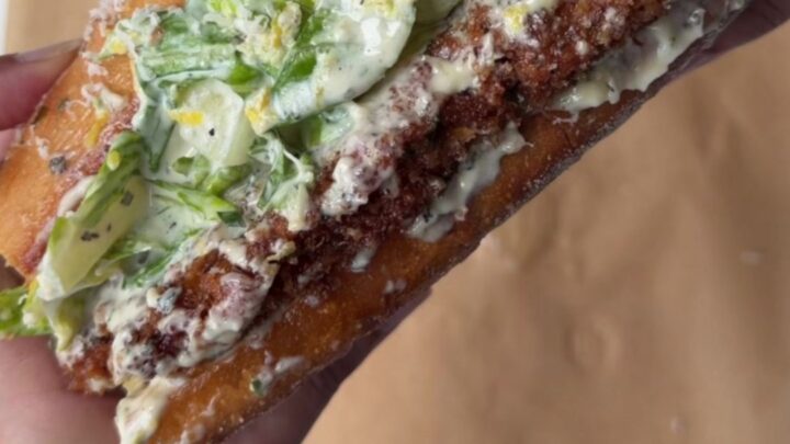 A crispy lemon herb chicken Caesar sandwich on toasted brioche, with romaine and parmesan visible.