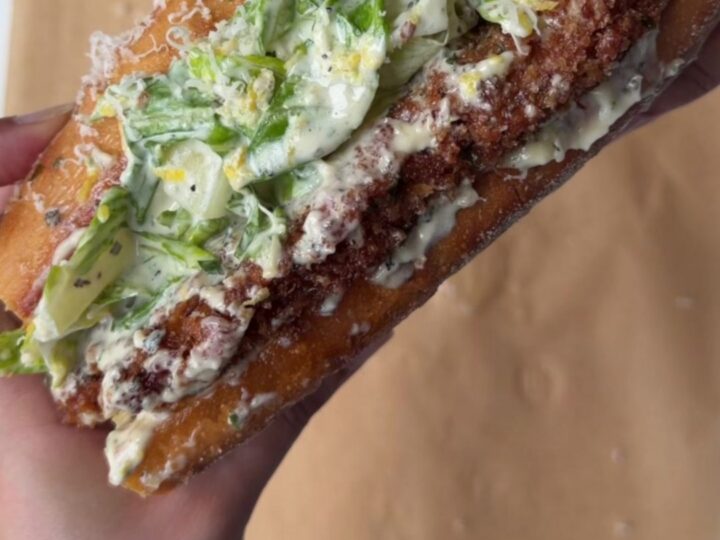 A crispy lemon herb chicken Caesar sandwich on toasted brioche, with romaine and parmesan visible.