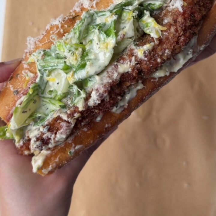 A crispy lemon herb chicken Caesar sandwich on toasted brioche, with romaine and parmesan visible.